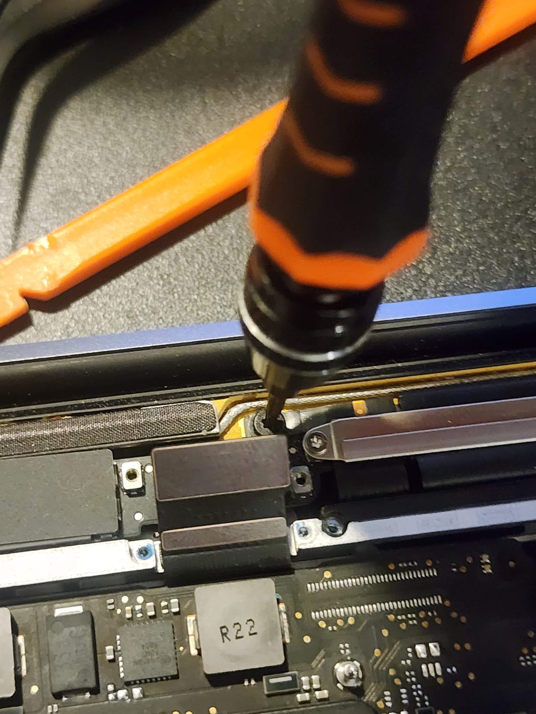 Close-up of a screwdriver removing a hinge screw during a laptop screen repair