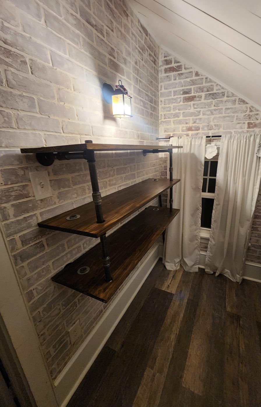 Custom pipe-and-timber shelving mounted on an exposed brick wall